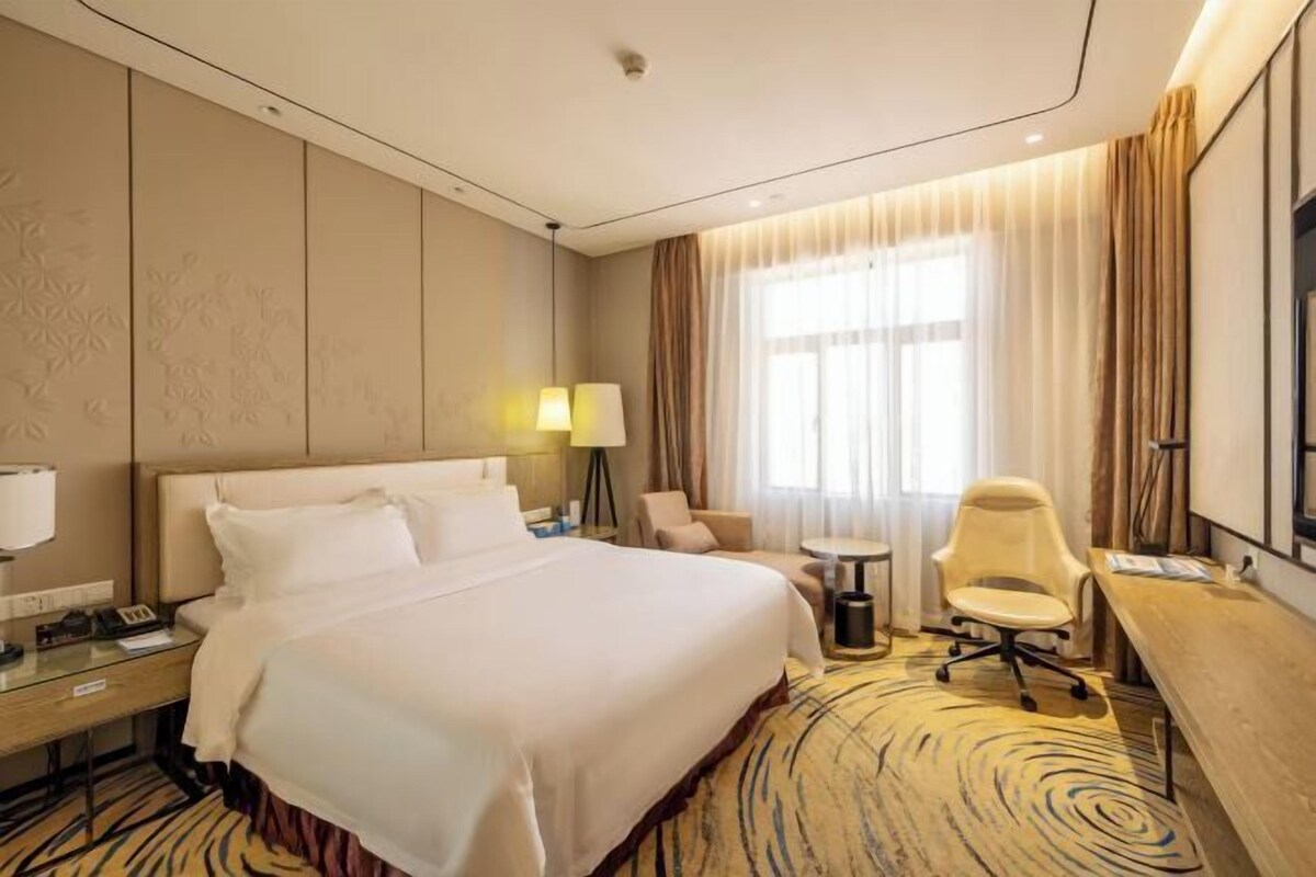 A hotel room with a large bed, a desk, a chair, a lamp, and a television.