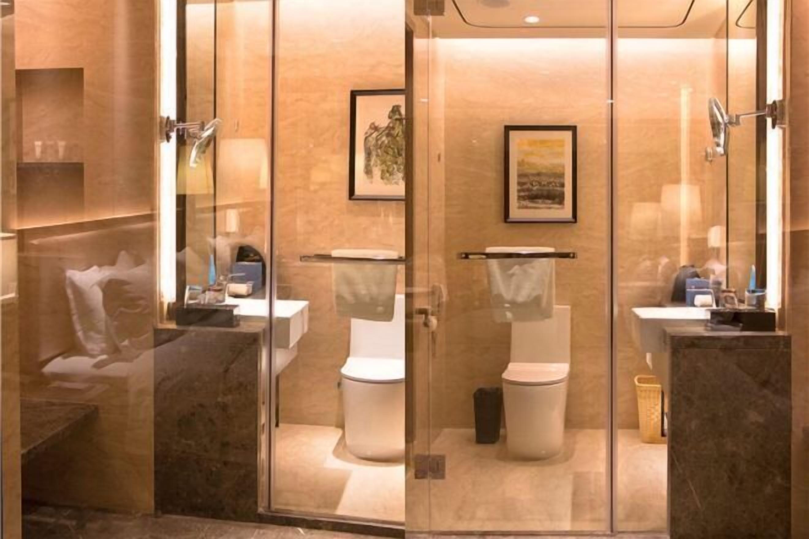 Un bagno moderno con pareti divisorie in vetro, due servizi igienici, un lavandino e opere d'arte incorniciate alle pareti.