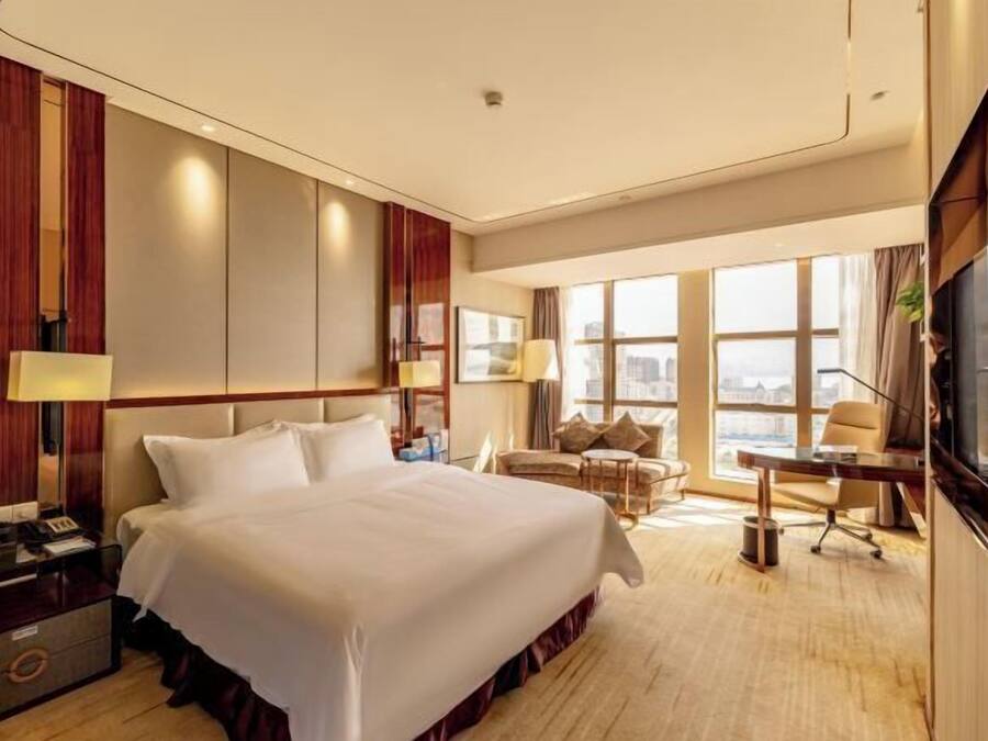 A hotel room with a large bed, a desk, a chair, and a TV.