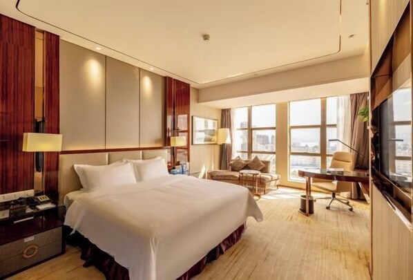 A hotel room with a large bed, a desk, a chair, and a TV. - Clear Lake Hotel (Shanwei)