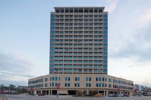 Un hotel de varios pisos con un patio central, que presenta un diseño moderno con techo plano y una combinación de fachada de vidrio y paneles sólidos.