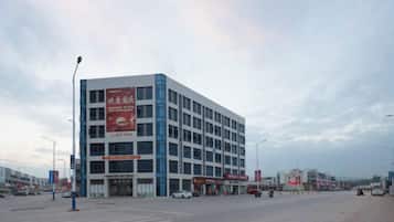 A multi-story building with a large sign on the side, a crosswalk in front, and a few cars parked nearby.