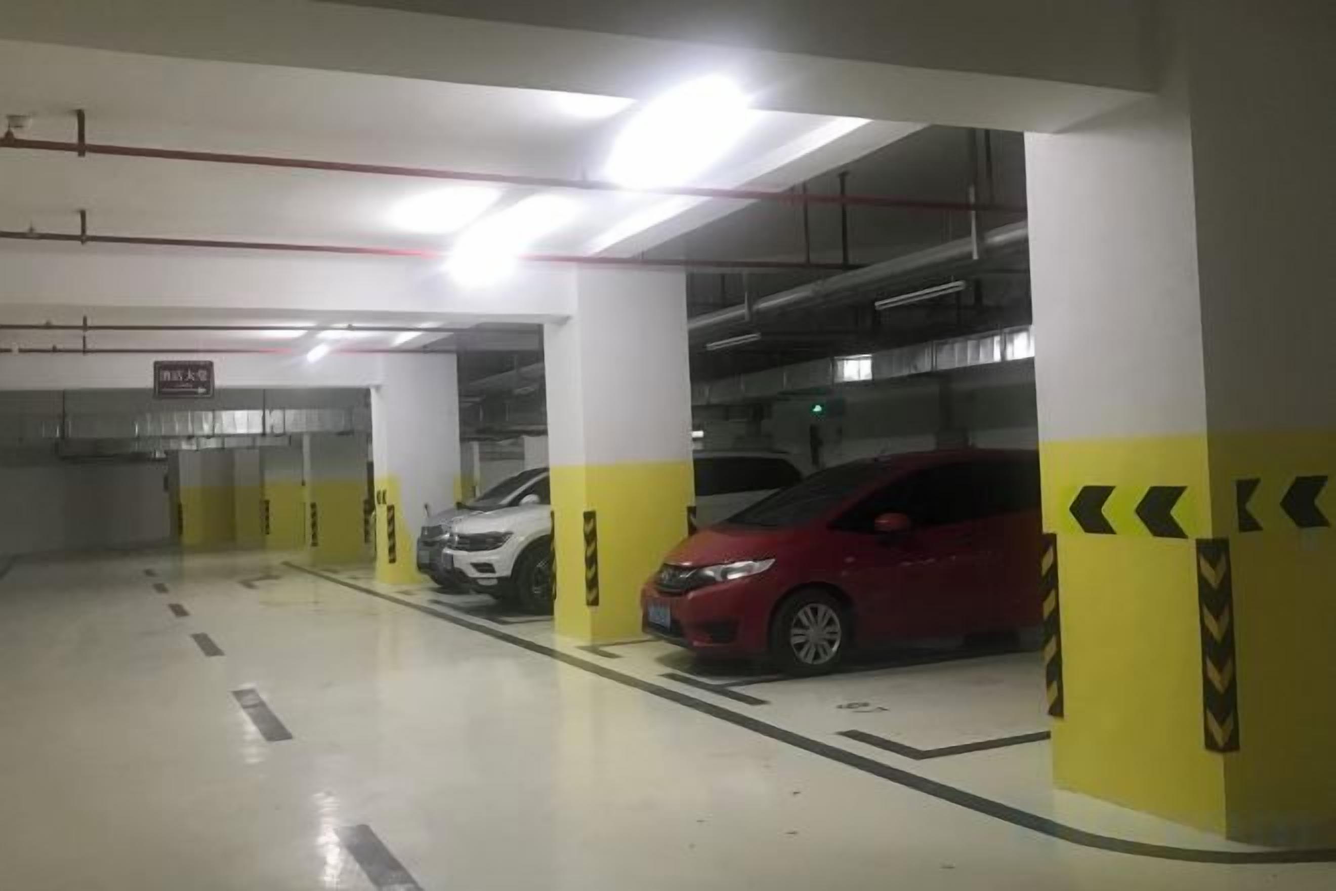 A parking garage with multiple parking spaces, yellow and white pillars, and a red car parked in one of the spaces.