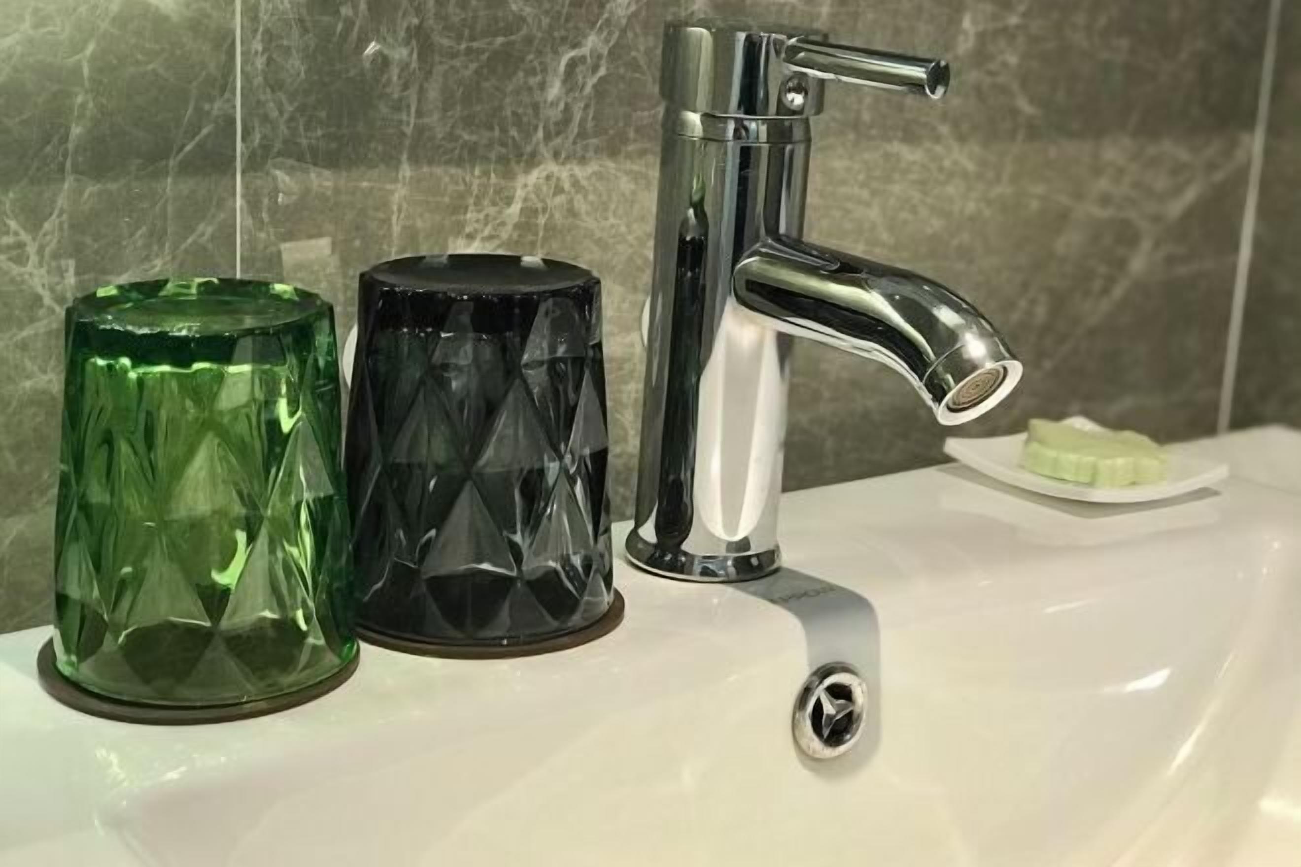 A bathroom sink with a chrome faucet, a green glass container, and a black glass container.