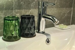 A bathroom sink with a chrome faucet, a green glass container, and a black glass container.