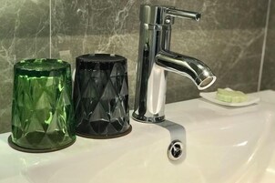 A bathroom sink with a chrome faucet, a green glass container, and a black glass container.