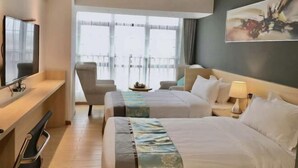 Quarto de hotel com duas camas, uma escrivaninha, uma cadeira, uma televisão e uma grande janela com vista para a varanda.