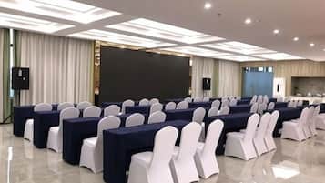 A conference room with rows of tables and chairs, a large screen, and a kitchen area.