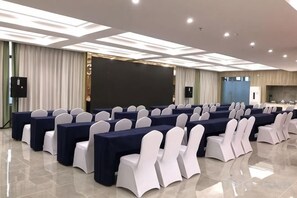A conference room with rows of tables and chairs, a large screen, and a kitchen area. - Mercure Styles Hotel Meizhou (Meizhou)