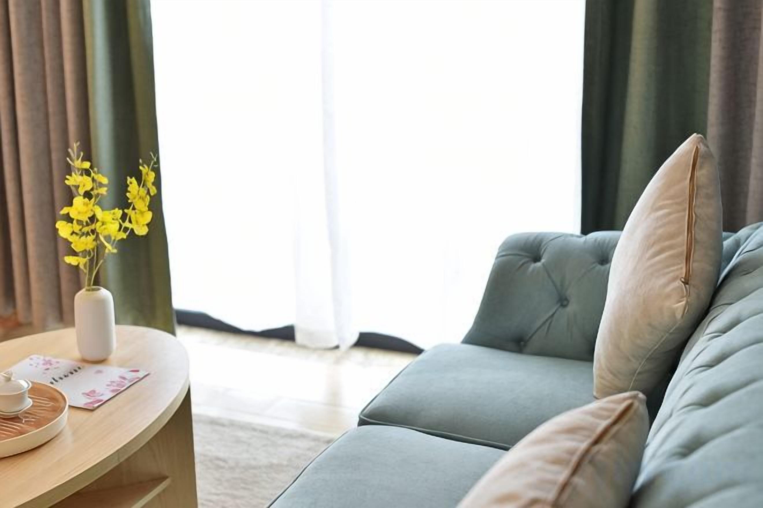 Een woonkamer met een bank, een bijzettafeltje met een bloemenvaas en een raam met gordijnen.