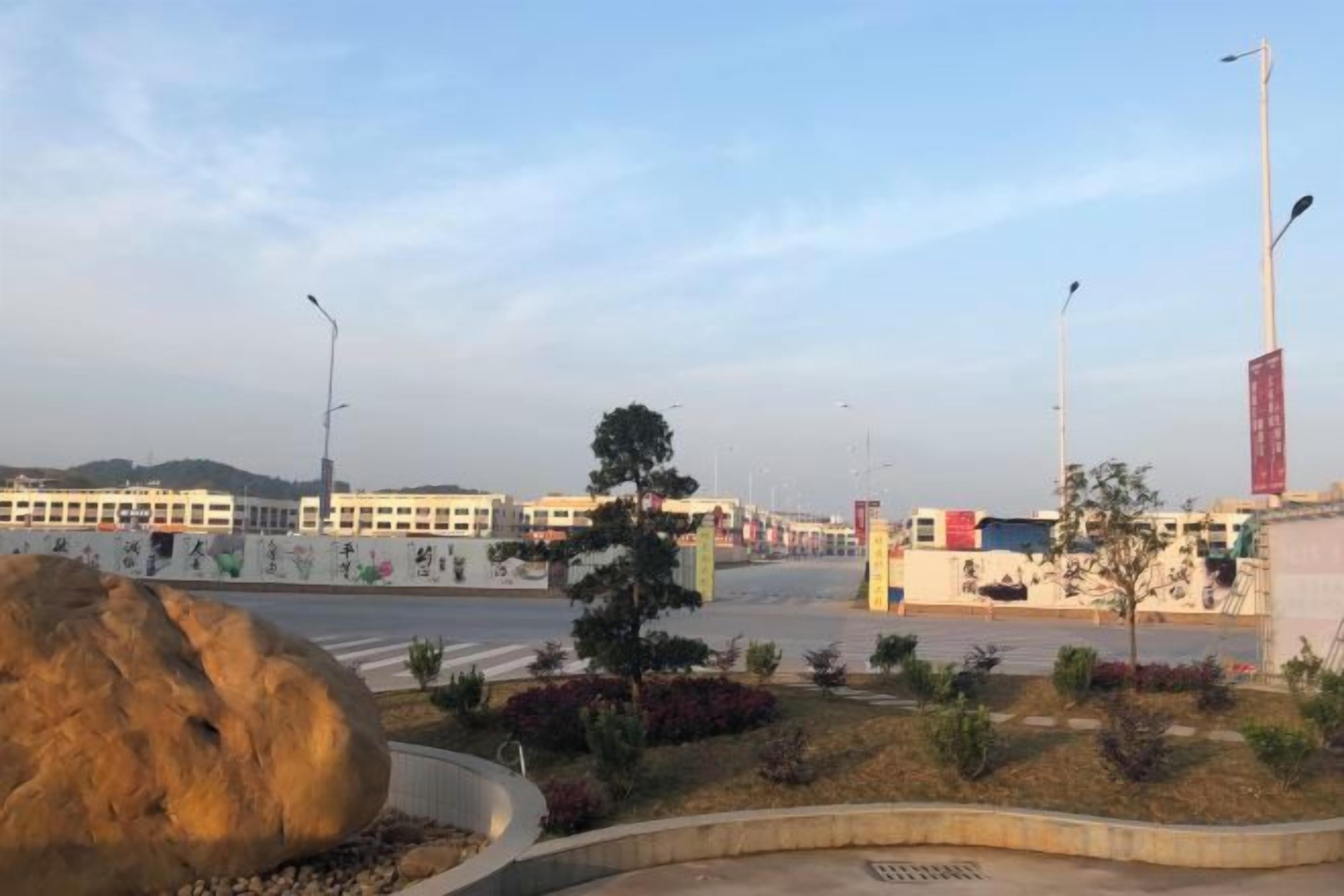 A roundabout with a large rock, a tree, and a building in the background.