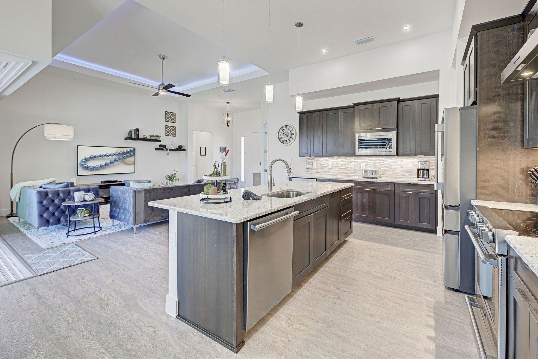 Una cocina moderna con armarios oscuros, una isla grande y un área de comedor con un sofá azul y una mesa de centro.