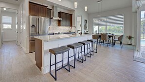 A modern kitchen with a central island, bar stools, and a dining area with a view. - Blue Pearl| Pool | Hot Tub | 3 Bed, 2 Bath (Rotonda West)