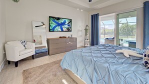 A bedroom with a large bed, a dresser, a sofa, a TV, and a balcony with a view. - Blue Pearl| Pool | Hot Tub | 3 Bed, 2 Bath (Rotonda West)