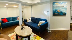 Un salon moderne avec un canapé bleu, une table basse ronde et un tableau représentant une jetée accroché au mur.