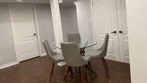 Un coin repas comprenant une table en verre et quatre chaises grises à revêtement en tissu, avec des pieds en bois.