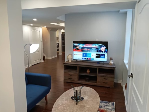 Uma sala de estar moderna com televisão de tela plana na parede, um sofá azul, uma mesa de centro e um armário de madeira sob a TV.