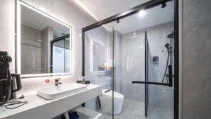 Un baño moderno con cabina de ducha de vidrio, un lavamanos blanco y un espejo.
