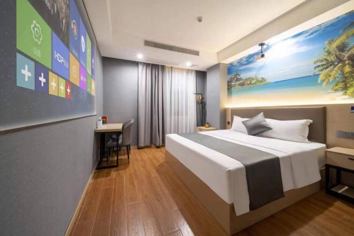 Une chambre d’hôtel comprenant un lit, un bureau, une chaise, une table de chevet et un mur orné d’une fresque aux motifs tropicaux.