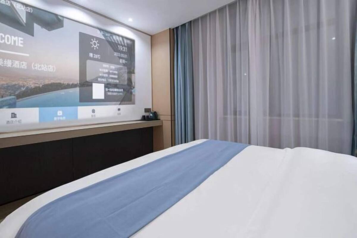 Une chambre d’hôtel avec un lit, une table de chevet, une grande affiche au mur et une fenêtre avec des rideaux.