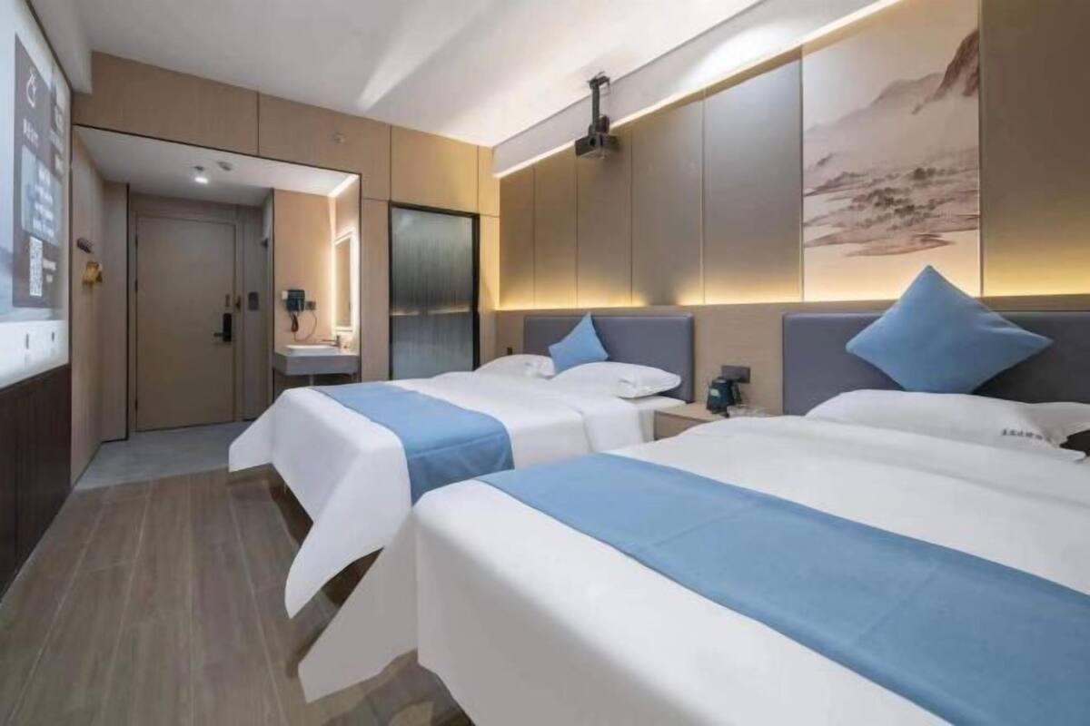 Une chambre d’hôtel avec deux lits, une salle de bain, un grand miroir et un projecteur fixé au mur.