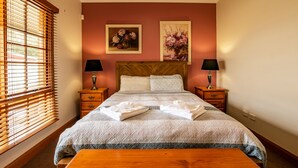 A neatly made bed with a quilted blanket, two bedside tables with lamps, and two framed floral paintings on the wall.