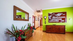 A hallway with a wooden cabinet, a mirror, a clock, and a decorative wall piece.