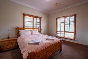 Un dormitorio con una cama de madera, dos mesitas de noche y dos ventanas con persianas.