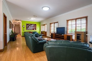 Una sala de estar con una pared verde, piso de madera, un juego de sofá, un televisor y un mueble de madera.