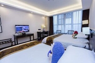 Habitación de hotel con dos camas, un escritorio con computadora, un televisor y un ventanal con cortinas.