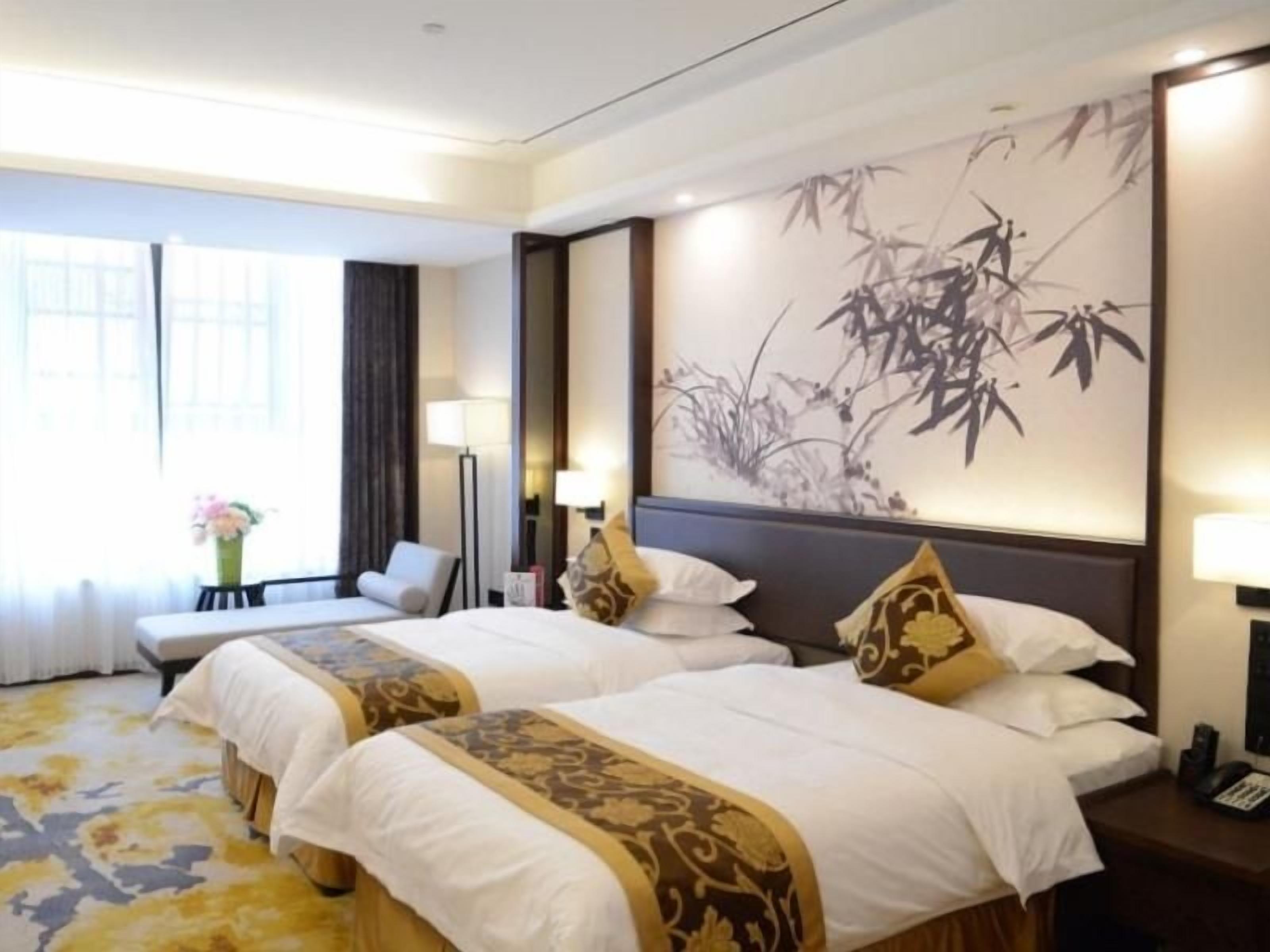 A hotel room with two beds, a sofa, a desk, and a large wall painting.
