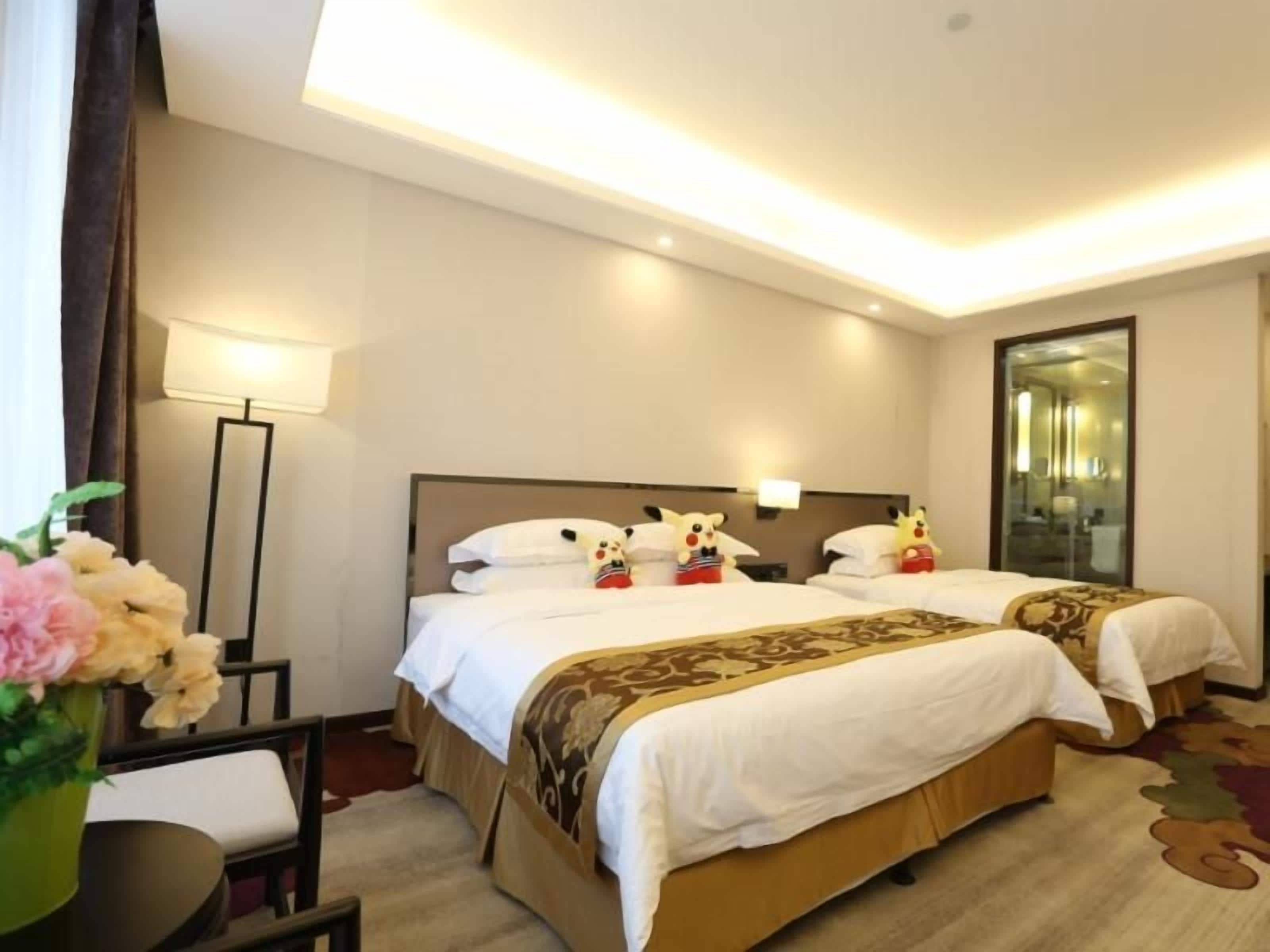 A hotel room with two beds, a bedside table, a lamp, and a mirror.