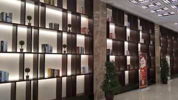 Un hall d’hôtel moderne avec un long comptoir d’accueil, un sol en marbre et un mur entier recouvert d’étagères à livres, agrémenté de plantes en pot.