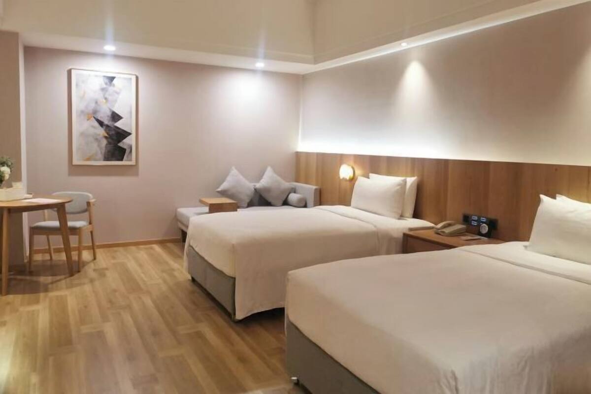 Une chambre d’hôtel avec deux lits, un plancher en bois, un bureau avec une chaise, une table de chevet avec une lampe et un tableau au mur.