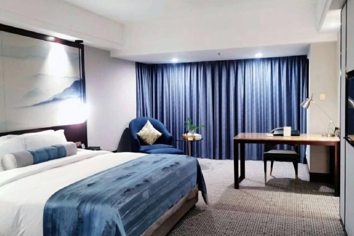 Une chambre d’hôtel avec un lit, un bureau, une chaise, une lampe et un rideau.
