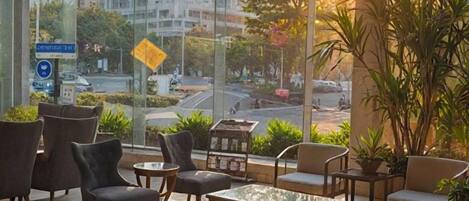 Un espace extérieur moderne aménagé avec des tables et des chaises, de grandes fenêtres offrant une vue sur la ville et des plantes en pot.