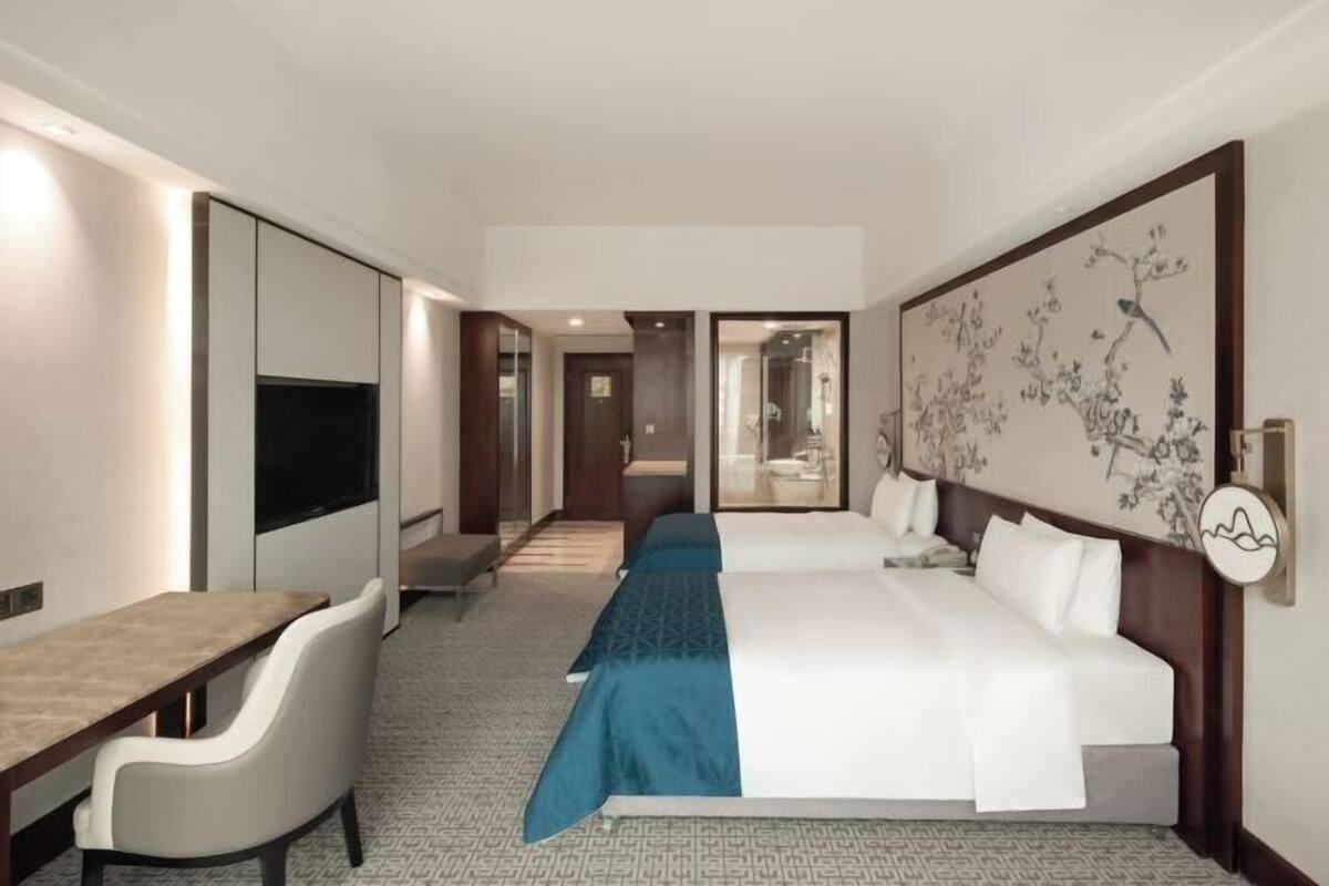 Une chambre d’hôtel équipée d’un lit, d’un bureau, d’une chaise, d’une télévision et ornée d’une grande œuvre d’art au mur.