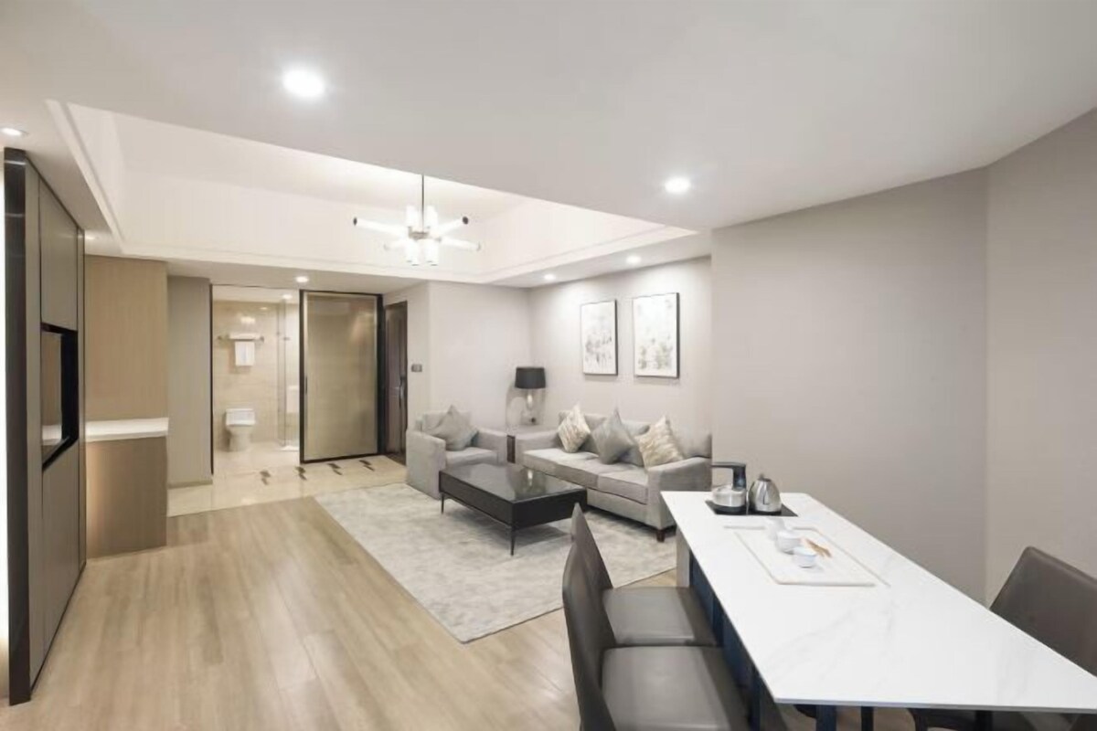 A modern living room with a sofa, coffee table, and dining table. There is a door leading to a bathroom and a ceiling fan.
