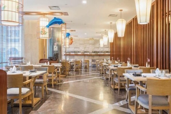 Un restaurante espacioso con mesas y sillas de madera, iluminación colgante y vistas a la ciudad a través de grandes ventanales.