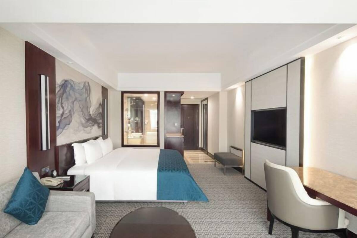 A modern hotel room with a large bed, a desk, a chair, and a TV.
