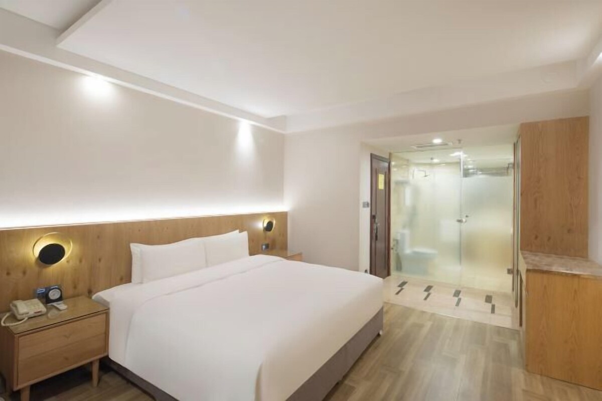A hotel room with a bed, bedside table, and a glass-enclosed shower area.