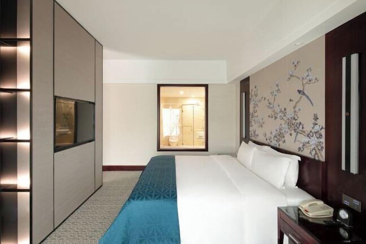 A hotel room with a large bed, a bedside table with a phone, and a view of the bathroom through a glass door.