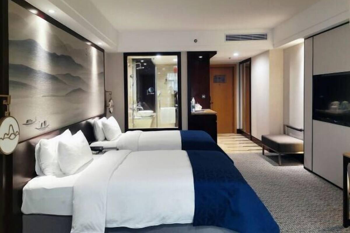 Une chambre d’hôtel avec deux lits, un grand tableau, une télévision et une salle de bain visible à travers une porte ouverte.