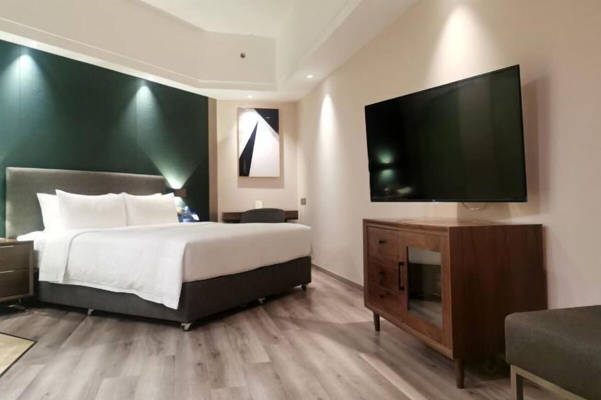 Une chambre d’hôtel moderne avec un grand lit, une table de chevet en bois, une télévision et une armoire en bois.