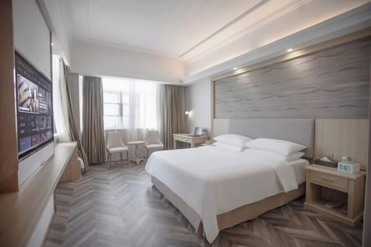 A hotel room with a large bed, a desk, two chairs, a TV, and a view of the outdoors.