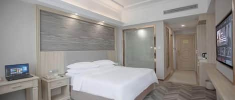 A hotel room with a bed, a desk, a laptop, a TV, and a door leading to another room.