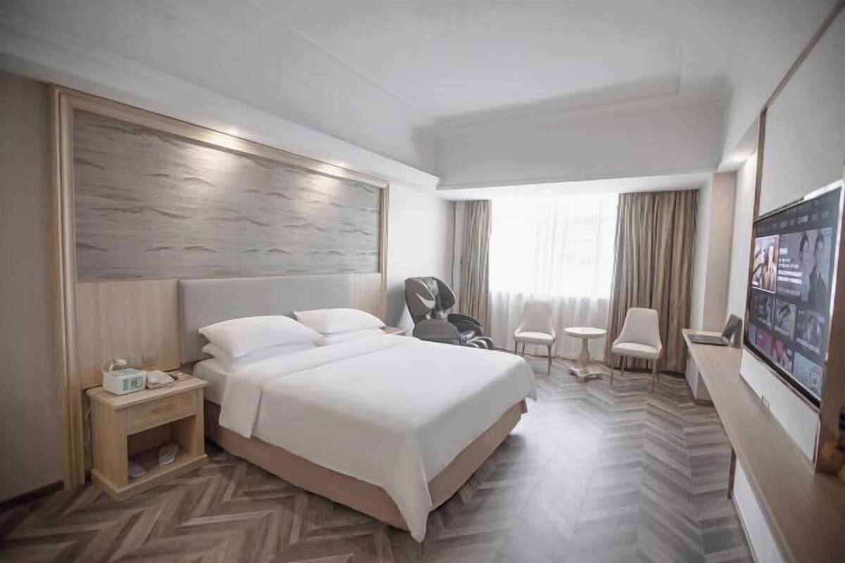 A hotel room with a large bed, a nightstand, a chair, a small table, and a TV.