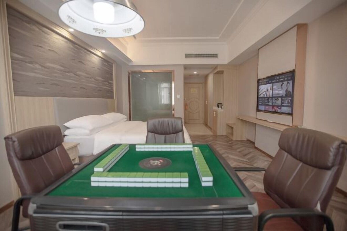A hotel room with a green snooker table, two leather chairs, a bed with white linens, a large poster on the wall, and a wooden textured wall.
