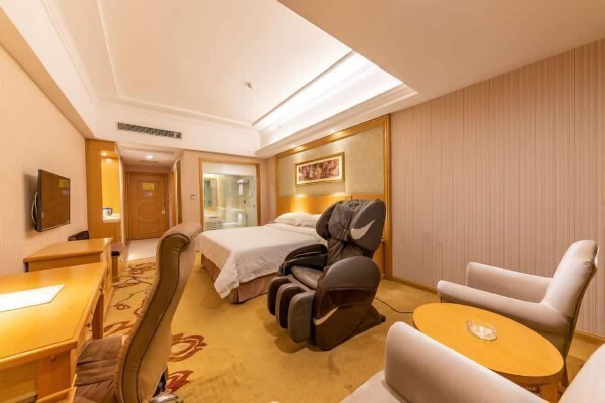 A hotel room with a bed, massage chair, sofa, and a small table.