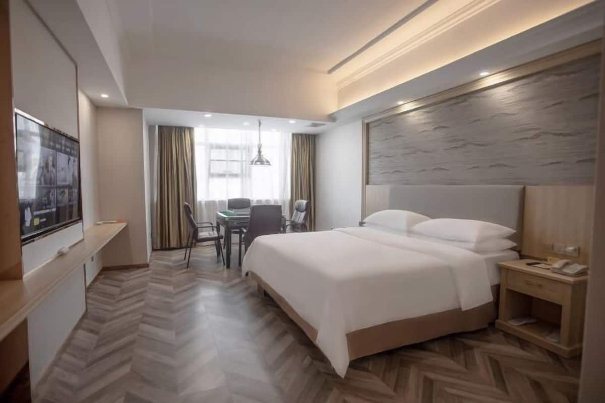 A hotel room with a large bed, a desk with a chair, a TV, and a wooden headboard.